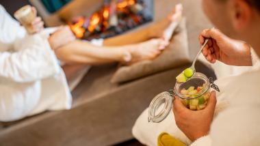 Entspannte Gäste im Bademantel beim Essen vor dem Kamin im Pfalzblick Wald Spa Resort