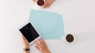 Tavolo con tovaglia blu e fiori, mare e spiaggia con ombrelloni sullo sfondo