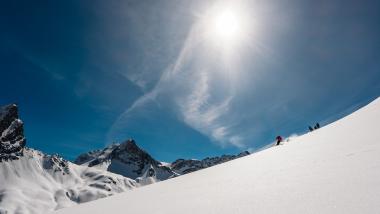 Ski fahren im Sonnenschein auf verschneitem Hang mit Hotel Aurora im Hintergrund
