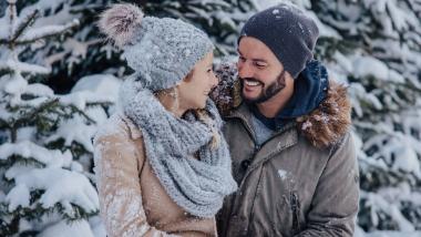 Ein glückliches Paar genießt den Winterurlaub beim Designer Motel Glockna in Fusch am Großglockner inmitten einer verschneiten Waldkulisse.