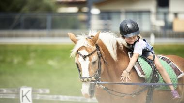 Kind reitet Pferd im Familienresort Buchau mit Helm und Freude