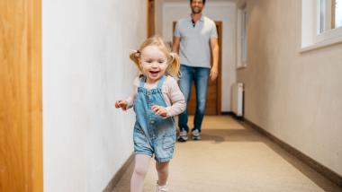 Fröhliches Kind läuft im Flur des Familienresort Buchau, Vater im Hintergrund