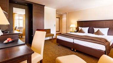 Helles Hotelzimmer mit Doppelbett und dunklen Holzmöbeln im Burghotel Staufeneck