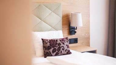 Der Dolomitenhof ***S gemütliches Hotelzimmer mit dekorativem Kissen und Wandlampe