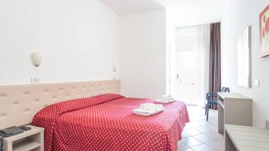 Camera d'albergo luminosa con letto matrimoniale e copriletto rosso a fiori