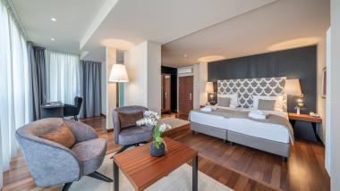 Modernes Zimmer im Hotel Mignon Meran Park & Spa mit Sitzbereich und Doppelbett.