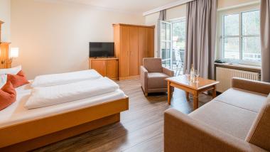 Hell eingerichtetes Zimmer im Hammerhof Bodenmais mit Bett, Sofa und TV