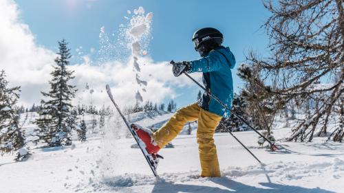 Skifahrer wirbelt Schnee auf einer sonnigen Piste beim Hotel Forstauerwirt auf
