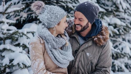 Ein glückliches Paar genießt den Winterurlaub beim Designer Motel Glockna in Fusch am Großglockner inmitten einer verschneiten Waldkulisse.