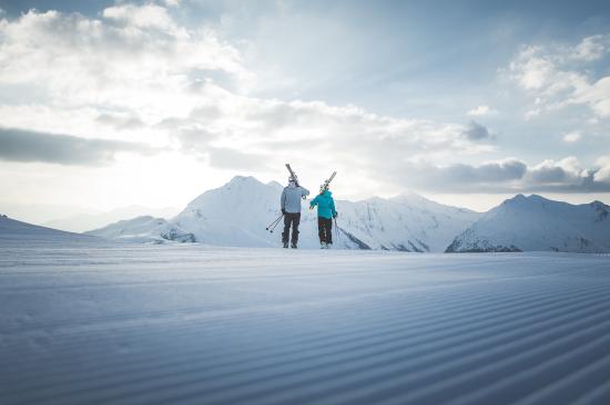 Zwei Skifahrer mit Skiern bei Hotel Seeber vor schneebedeckten Bergen