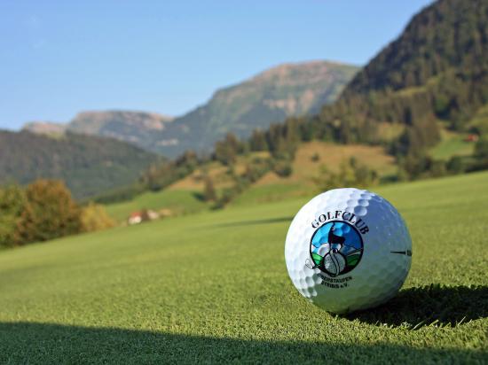 Golf ball on green grass with Allgäu mountains and sun in the background