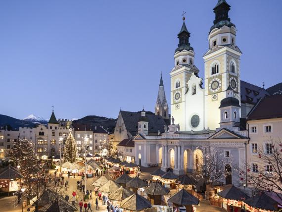 Laurena: Weihnachtsmarkt mit beleuchteter Kirche mit zwei Türmen in der Dämmerung