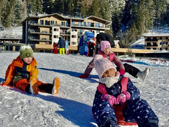 Kinder rodeln im Schnee vor dem Familienresort Buchau in winterlicher Waldlandschaft