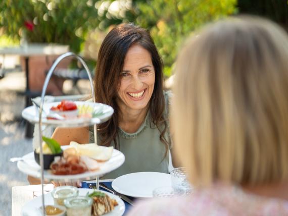 Zwei Frauen beim Essen auf der Terrasse von Castel Sallegg mit mehrstöckiger Platte