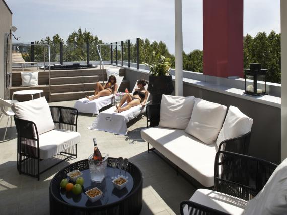 Terrazza sul tetto dell'Q Hotel con lettini, divani da giardino e due persone che prendono il sole