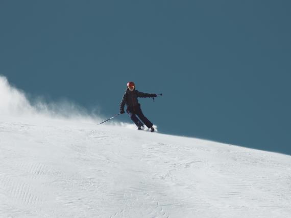Der Greil Skifahrer fährt schnell einen schneebedeckten Hang hinunter vor klarem Himmel