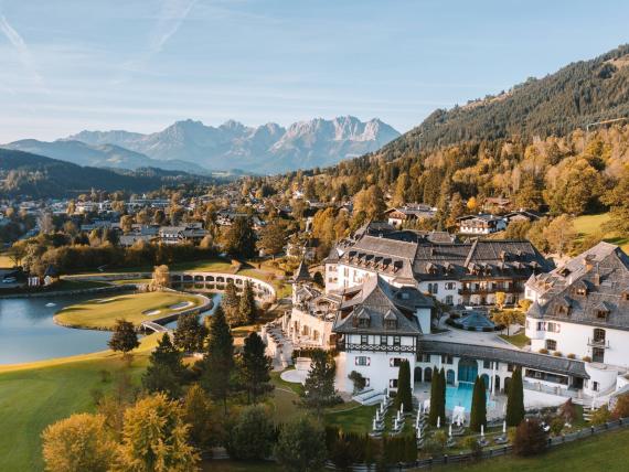 Schlosshotel Kitzbühel beside a lake, with autumn-colored mountains in the background
