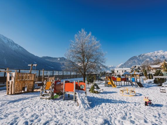 Verschneiter Spielplatz im Familienresort Buchau vor schneebedeckten Bergen