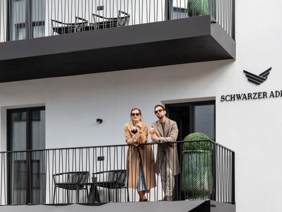 Zwei Personen auf einem Balkon neben dem Schriftzug Schwarzer Adler
