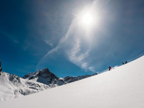 Ski fahren im Sonnenschein auf verschneitem Hang mit Hotel Aurora im Hintergrund