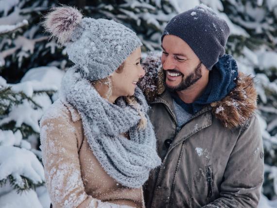 Ein glückliches Paar genießt den Winterurlaub beim Designer Motel Glockna in Fusch am Großglockner inmitten einer verschneiten Waldkulisse.