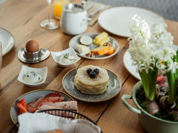 Frühstückstisch mit Ei, Käse, Aufstrich, Wurst, Kaffee, Pancakes und einem Glas Orangensaft