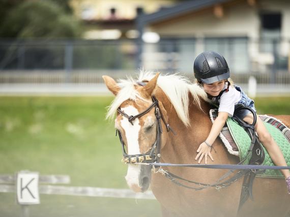 Kind reitet Pferd im Familienresort Buchau mit Helm und Freude