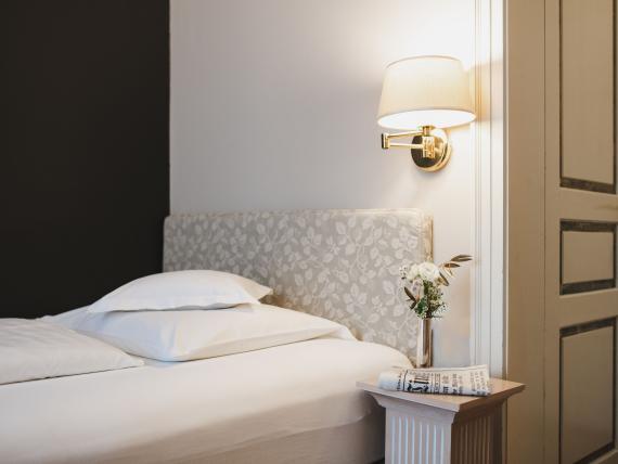 Cozy single bed at Hotel Adria with wall lamp and flowers on bedside table