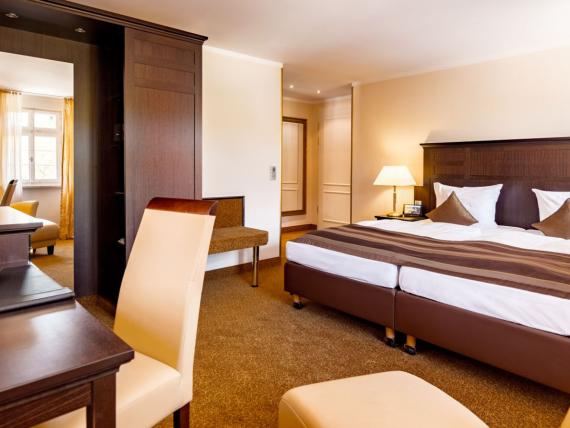 Helles Hotelzimmer mit Doppelbett und dunklen Holzmöbeln im Burghotel Staufeneck