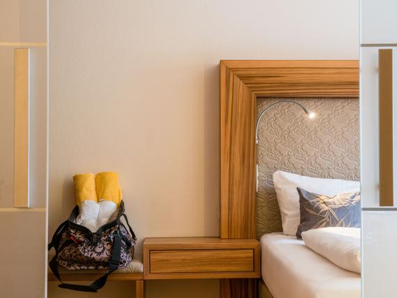 Modernes Hotelzimmer im Hammerhof Bodenmais mit Bett und Tasche auf Bank
