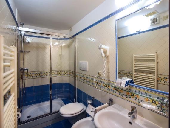 Bagno con doccia all'Hotel Amalfi, piastrelle blu e bianche con asciugacapelli