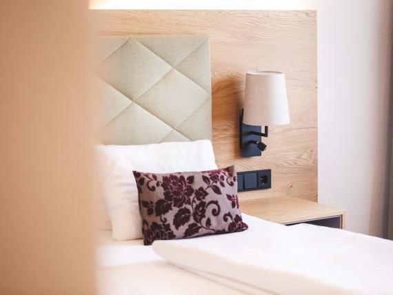 Der Dolomitenhof ***S gemütliches Hotelzimmer mit dekorativem Kissen und Wandlampe