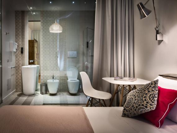 Camera del Teku Boutique Hotel con letto, angolo salotto e bagno a vista dietro una vetrata