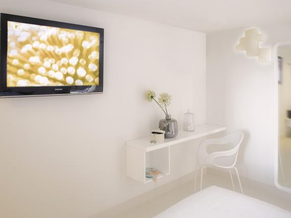 Camera moderna al Q Hotel con TV, scrivania e sedia bianca