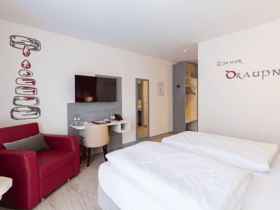 Modernes Hotelzimmer mit Doppelbett und rotem Sessel im Mythenresort Heimdall
