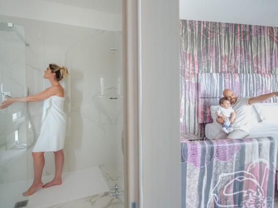 Donna nella doccia e uomo con bambino sul letto nella camera del Bibione Palace Hotel