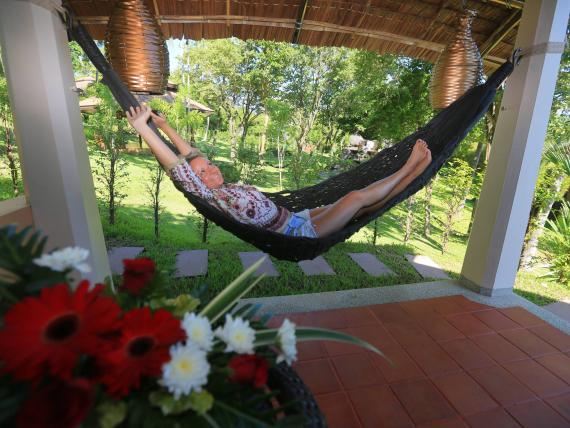 Person relaxing in a hammock at The Mangosteen Ayurveda & Wellness Resort patio.