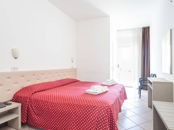 Camera d'albergo luminosa con letto matrimoniale e copriletto rosso a fiori