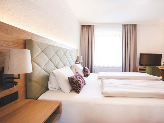 Der Dolomitenhof ***S modernes Hotelzimmer mit zwei Betten und TV