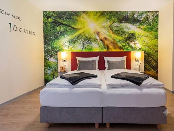 Gemütliches Doppelbett im Zimmer Jötunn im Mythenresort Heimdall mit Waldwandbild