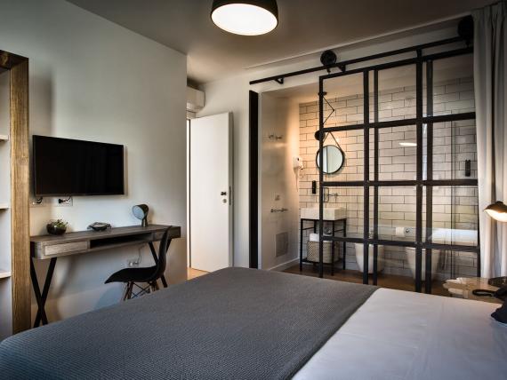 Camera del Teku Boutique Hotel con letto, scrivania e bagno dietro una parete divisoria in vetro nero