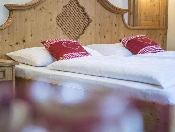 Gemütliches Doppelbett im Hotel Waldsee mit Holzverkleidung und roten Kissen