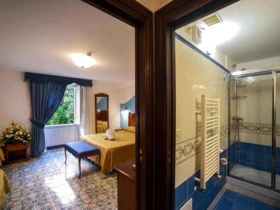Camera doppia Hotel Amalfi con bagno, tende blu e pavimenti piastrellati