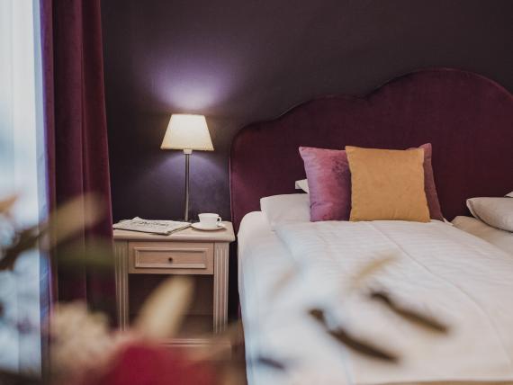 Cozy hotel room at Hotel Adria with purple headboard and bedside lamp