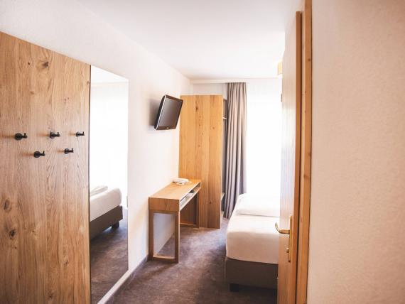 Der Dolomitenhof ***S helles Hotelzimmer mit Holzmöbeln und TV