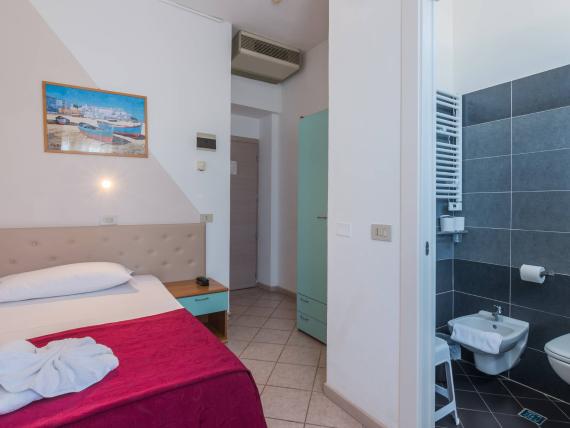 Camera d'albergo con copriletto rosso e quadro di fiori sulla parete