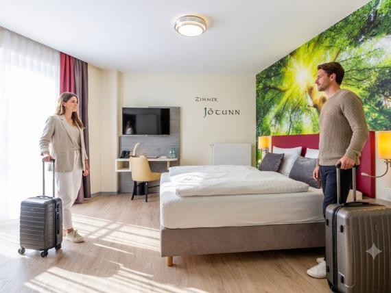Paar mit Koffern im hellen Zimmer Jöcunn im Mythenresort Heimdall