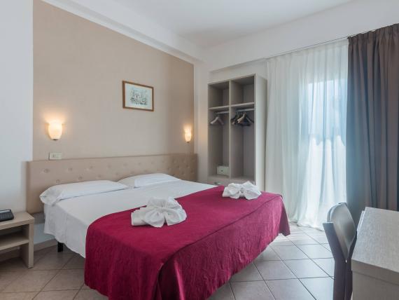 Camera d'albergo con asciugamani a forma di fiori sul letto e copriletto rosso