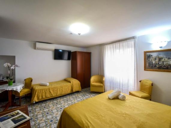 Camera dell'Hotel Amalfi con letti e sedie gialle, TV e finestra con tende
