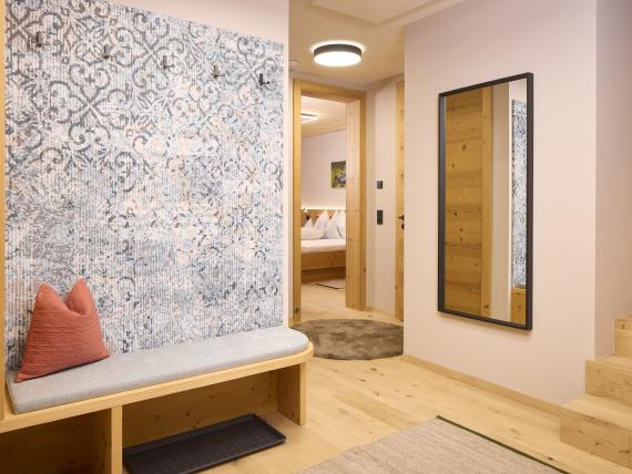 Hochfeldhof Flur mit Holzbank, Kissen, Spiegel und Eingang zu Schlafzimmer